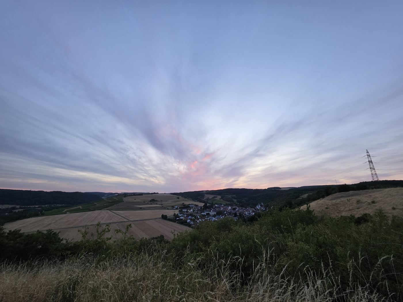 Dämmerungspanorama über Felder und Dorf im Tal, rosa Wolken
