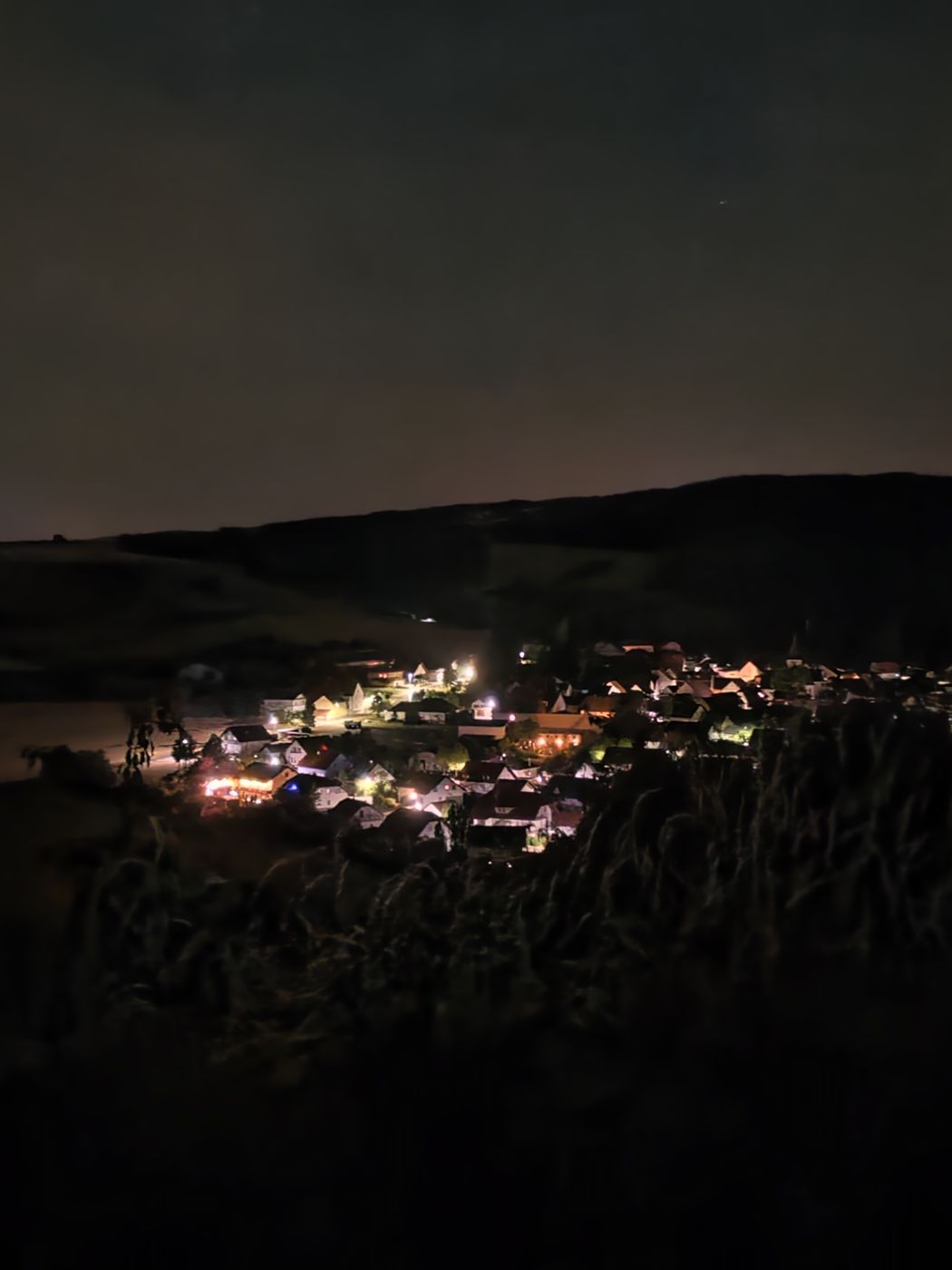 Das Dorf bei Nacht, warme Lichter zwischen dunklen Hügeln