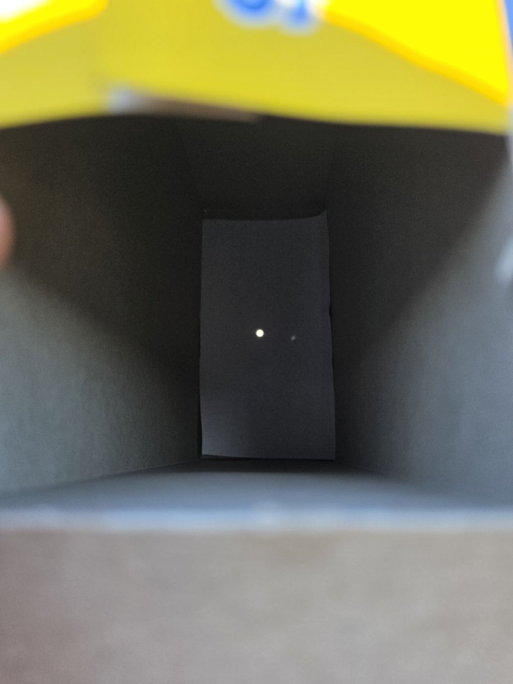 Blick in die dunkle Müslipackung, auf der schwarzen Rückwand ein kleiner runder heller Punkt: das projizierte Sonnenbild