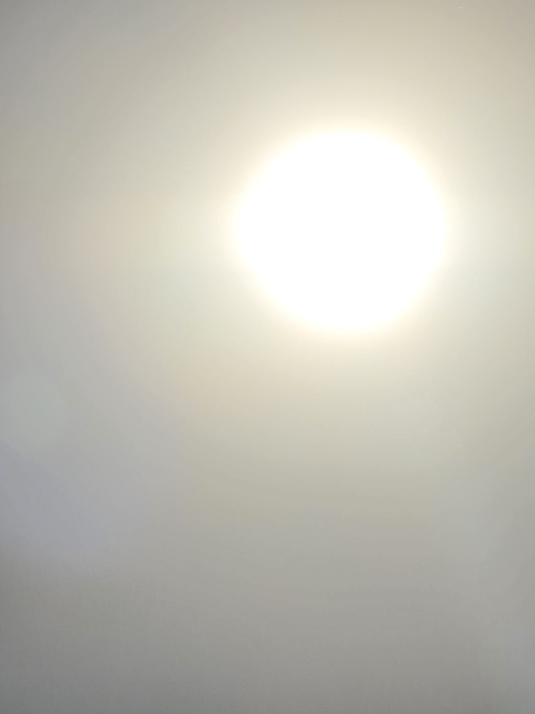 Stark überstrahlte Sonne am dunstigen Abendhimmel, nur ein gleißender heller Fleck