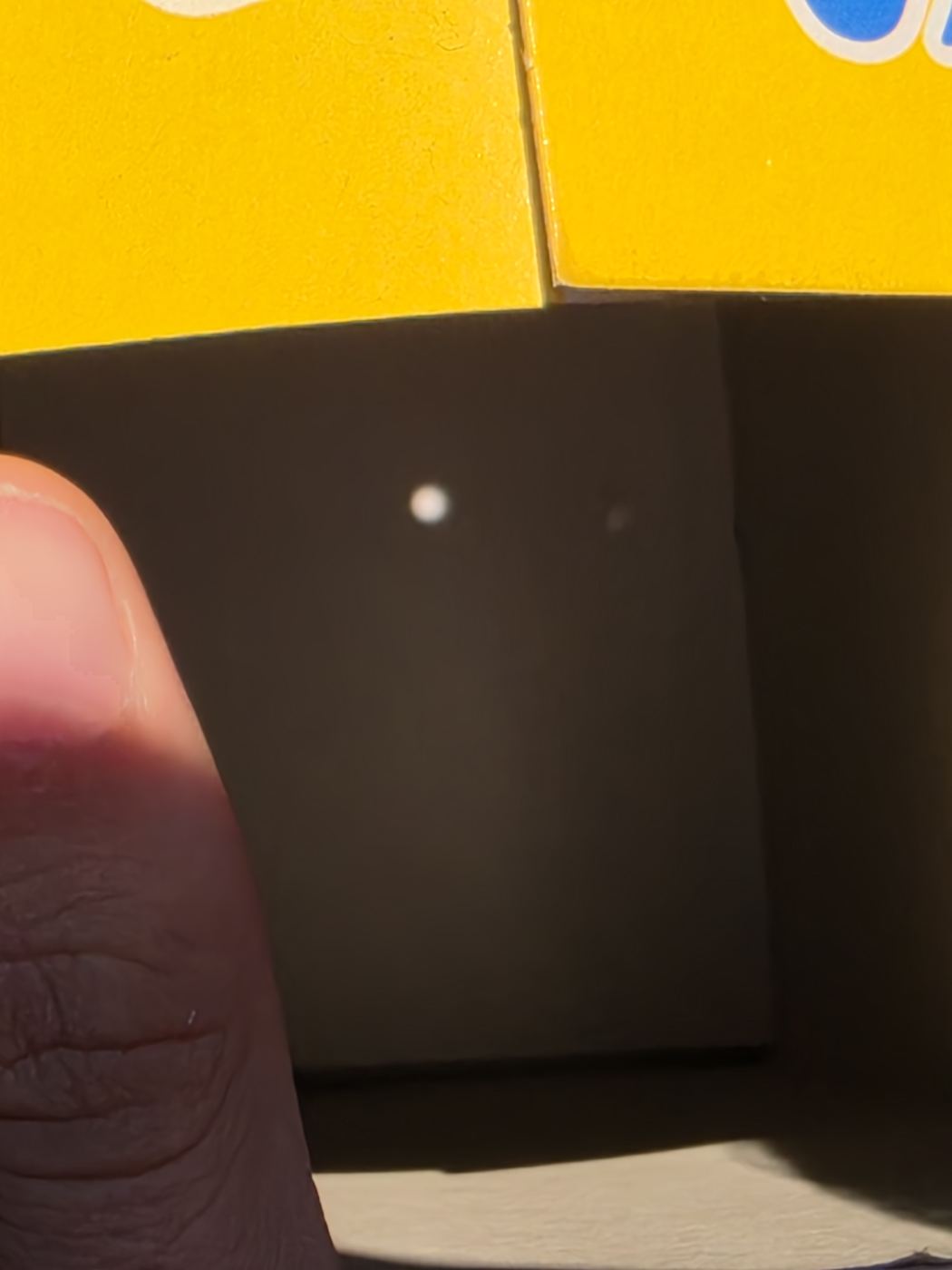 Nahaufnahme der Projektionswand in der Müslipackung mit kleinem hellem Sonnen-Punkt, unten ein Daumen im Bild