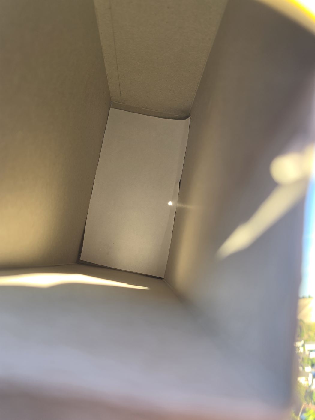 Blick in einen großen Karton mit weißem Blatt als Projektionsfläche, darauf ein kleiner heller Sonnen-Punkt