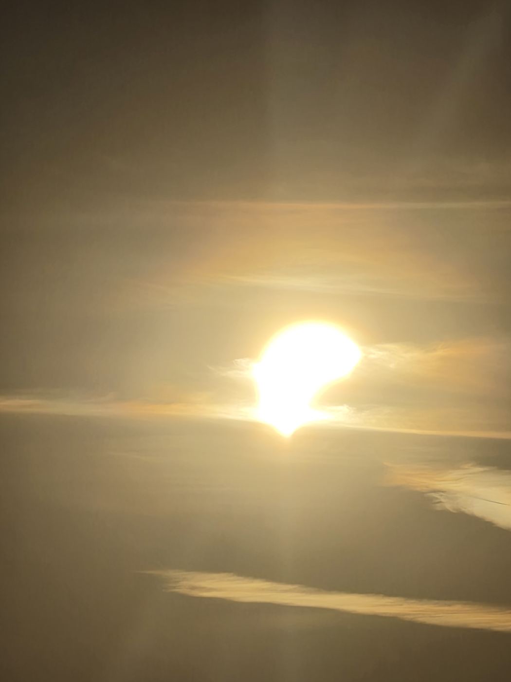 Die tief stehende Sonne hinter Dunstschleiern, deutlich sichtbar fehlt der Scheibe ein großes Stück, der Mond schiebt sich davor