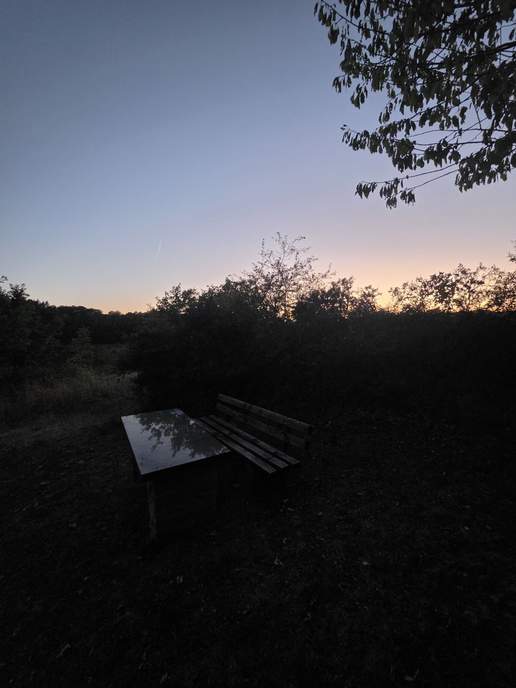 Bank mit Tisch an einem Aussichtspunkt in der blauen Stunde, hinter dem Höhenzug glimmt das letzte Orange des Sonnenuntergangs