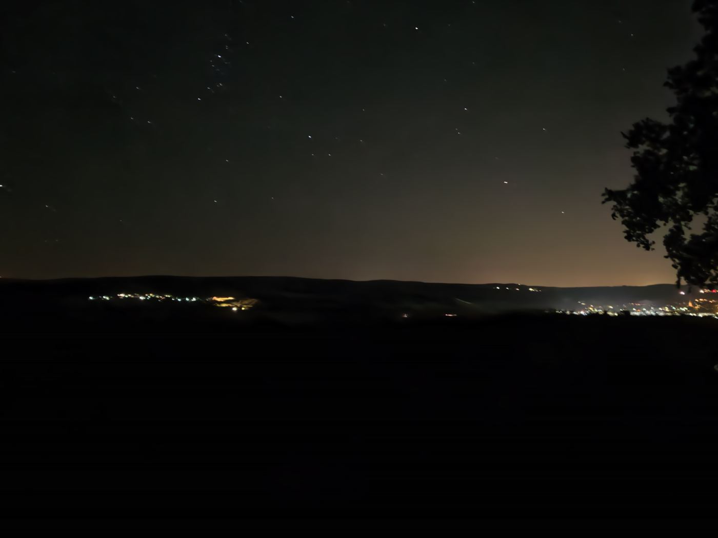 Nachthimmel voller Sterne über dem dunklen Nahetal, unten die Lichter der Dörfer, rechts eine Baumsilhouette